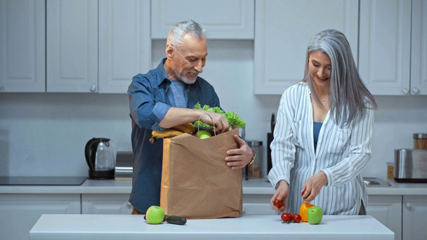 ηλικιωμένο και διαφυλετικό ζευγάρι που βάζει φρούτα και λαχανικά στο τραπέζι  - Πλάνα, βίντεο