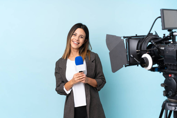 Femme journaliste tenant un microphone et rapportant des nouvelles sur fond bleu isolé applaudissant
 - Photo, image