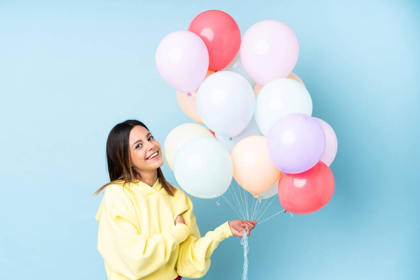 Frau hält Luftballons auf einer Party vor isoliertem blauen Hintergrund und lacht - Foto, Bild