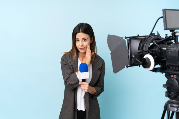 Mulher repórter segurando um microfone e relatando notícias sobre fundo azul isolado sussurrando algo
 - Foto, Imagem