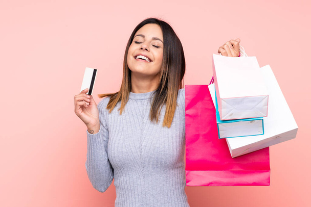 Женщина на изолированном розовом фоне держит сумки с покупками и кредитку - Фото, изображение
