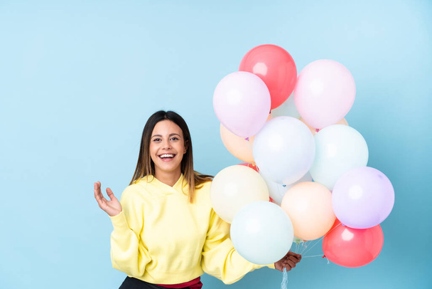 Woman holding balloons in a party over isolated blue background laughing - Foto, Imagen
