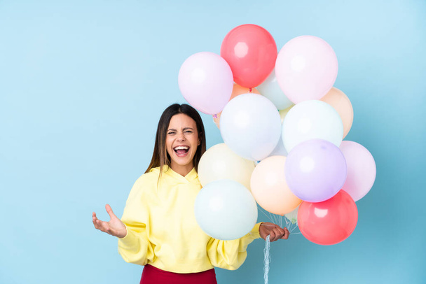 Frau hält Luftballons in einer Party über isoliertem blauem Hintergrund unglücklich und frustriert über etwas - Foto, Bild
