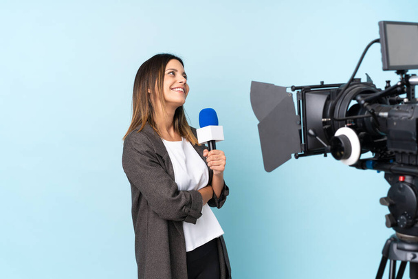 レポーターの女性がマイクを持って孤立した青い背景の上にニュースを報告笑い - 写真・画像