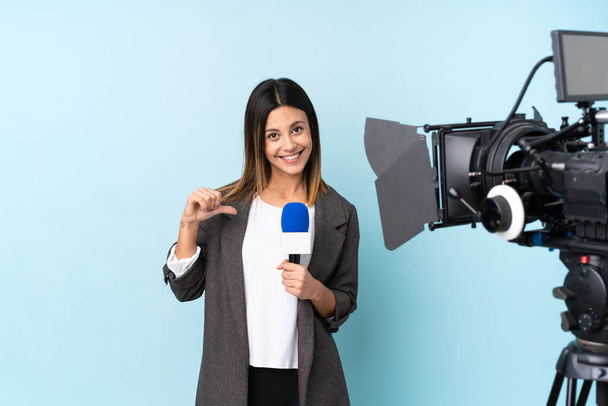 Reporter woman holding a microphone and reporting news over isolated blue background proud and self-satisfied - Photo, Image