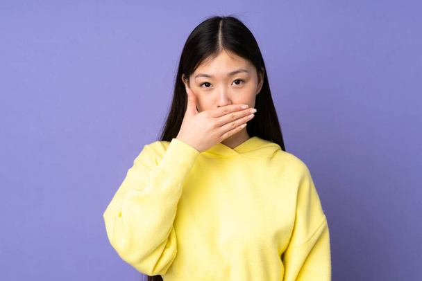 Jeune femme asiatique isolé sur fond violet couvrant la bouche avec la main
 - Photo, image