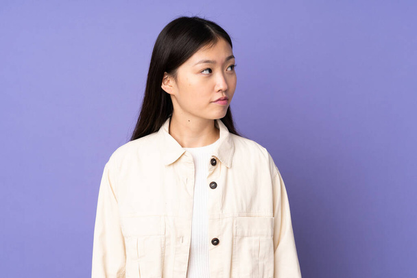 jonge aziatische vrouw geïsoleerd op paarse achtergrond op zoek naar de zijkant - Foto, afbeelding