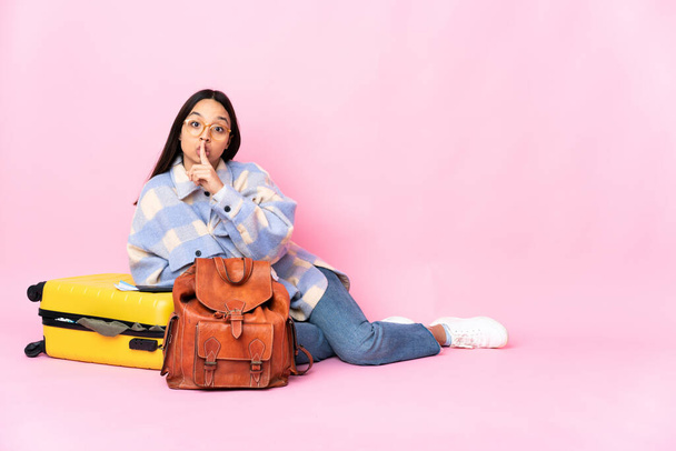 Viaggiatore donna con una valigia seduta sul pavimento che mostra un segno di silenzio gesto mettendo il dito in bocca
 - Foto, immagini