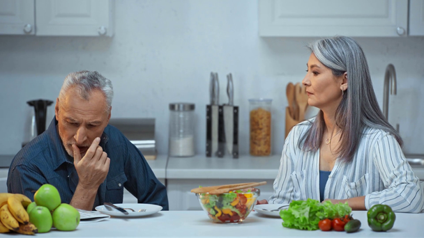 senior interracial pár mluví v blízkosti salátu v kuchyni  - Záběry, video