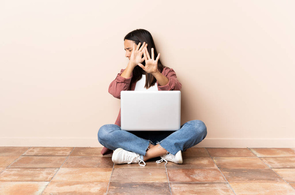 Young mixed race woman with a laptop sitting on the floor nervous stretching hands to the front - Foto, imagen