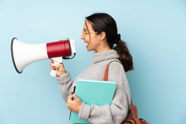 Young mixed race woman going to school isolated on blue background shouting through a megaphone - Foto, Bild