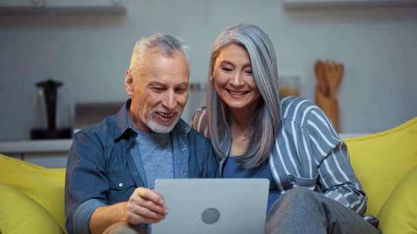 ηλικιωμένο διαφυλετικό ζευγάρι κουνώντας τα χέρια και κοιτάζοντας το φορητό υπολογιστή  - Πλάνα, βίντεο