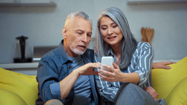 senior interracial pareja saludando manos y mirando en smartphone
  - Imágenes, Vídeo