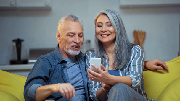 ηλικιωμένο διαφυλετικό ζευγάρι γελώντας και κοιτάζοντας smartphone  - Πλάνα, βίντεο