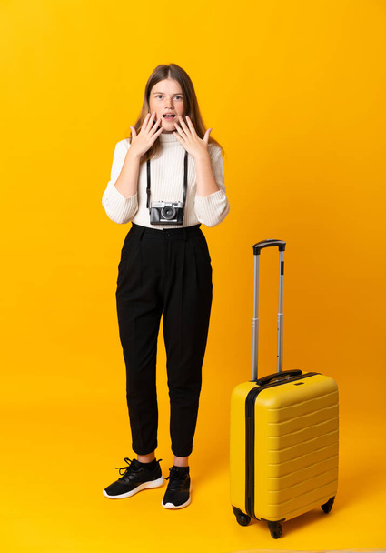 Πλήρες σώμα του ταξιδιώτη έφηβος κορίτσι με βαλίτσα πάνω από απομονωμένο κίτρινο φόντο με έκπληξη προσώπου έκφραση - Φωτογραφία, εικόνα