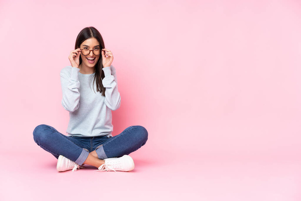 Young caucasian woman isolated on pink background with glasses and surprised - 写真・画像