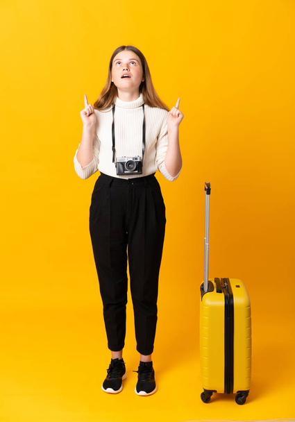 Full body of traveler teenager girl with suitcase over isolated yellow background pointing with the index finger a great idea - Foto, Imagem