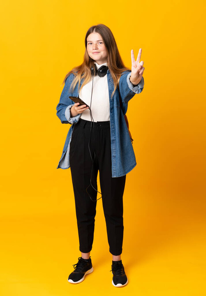 Студентка украинской девочки-подростка на изолированном желтом фоне улыбается и показывает знак победы
 - Фото, изображение