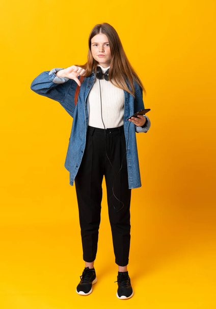 Diák ukrán tinédzser lány izolált sárga háttér mutatja hüvelykujj lefelé jel - Fotó, kép