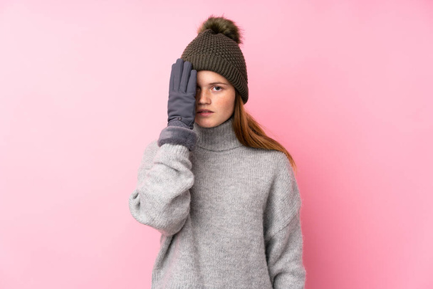 Ukrainian teenager girl with winter hat over isolated pink background covering a eye by hand - Foto, immagini