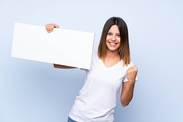 junge Frau über isoliertem blauem Hintergrund mit einem leeren weißen Plakat zum Einfügen eines Konzepts - Foto, Bild