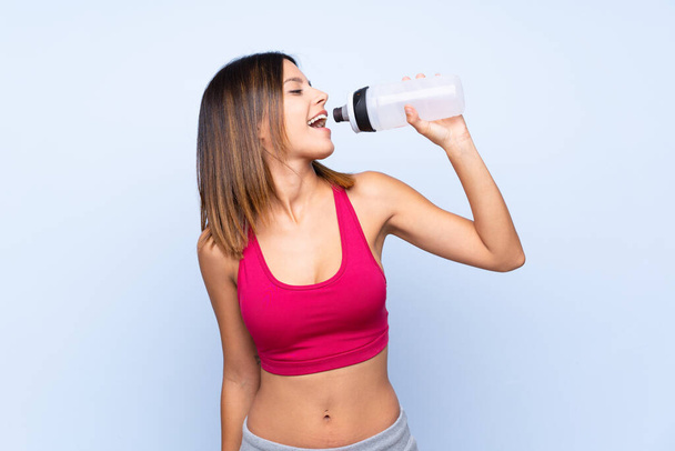 Jonge sport vrouw over geïsoleerde blauwe achtergrond met sport water fles - Foto, afbeelding