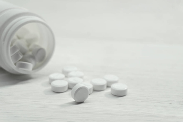 pillole mediche versato da una bottiglia bianca sul tavolo bianco - Foto, immagini