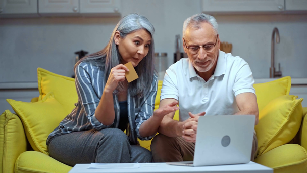 Senior interracial paar online shopping in der Nähe von laptop im Wohnzimmer  - Filmmaterial, Video