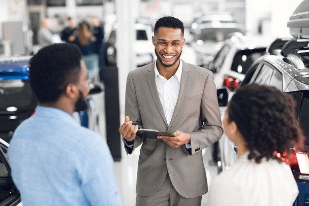 Professioneller Händler im Gespräch mit Kunden, die Autos im Autohaus zeigen - Foto, Bild