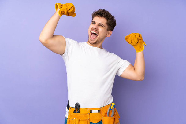 Young electrician man over isolated on purple background celebrating a victory - Fotoğraf, Görsel