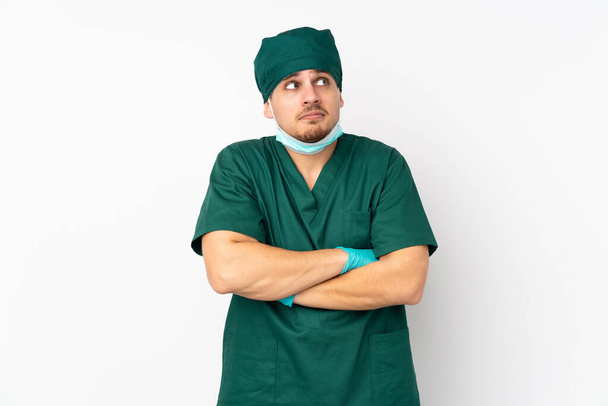 Cirujano en uniforme verde aislado sobre fondo blanco aislado haciendo gestos de dudas mientras levanta los hombros
 - Foto, imagen