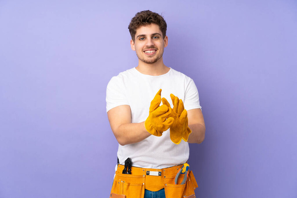 Mladý elektrikář muž nad izolované na fialové pozadí aplauding - Fotografie, Obrázek