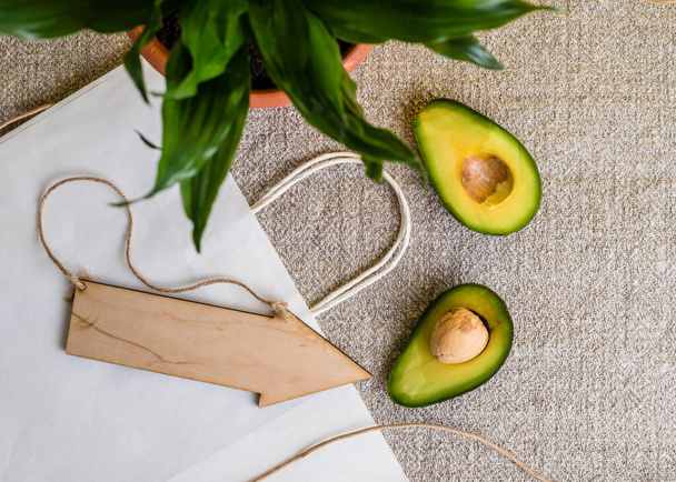 Set of eco friendly kitchen items. wooden cutlery, glassware, a flower in a ceramic pot, natural oils and a sliced avocado on a linen tablecloth against a yellow wall. Zero waste and plastic free - Photo, Image