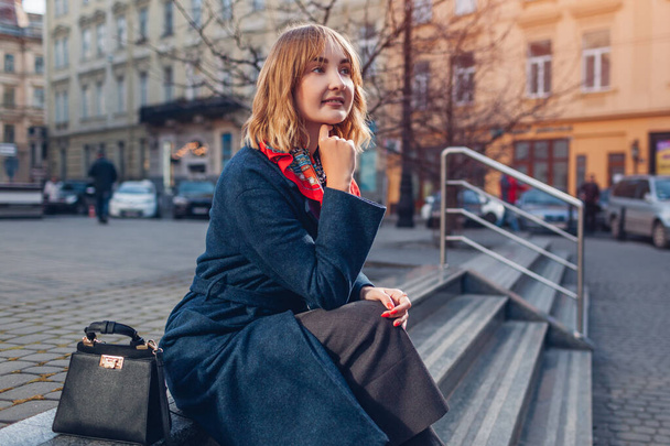 Retrato de una mujer joven con estilo que usa una bufanda de abrigo azul que relaja con un bolso de mano al aire libre en la calle de la ciudad. Moda de primavera accesorios femeninos. Traje de moda
 - Foto, imagen