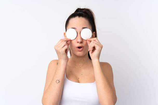 Mladá brunetka žena přes izolované bílé pozadí s bavlněnou podložkou pro odstranění make-upu z obličeje - Fotografie, Obrázek