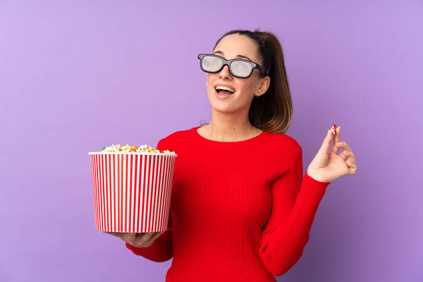 Jeune femme brune sur fond violet isolé avec des lunettes 3D et tenant un grand seau de popcorns
 - Photo, image
