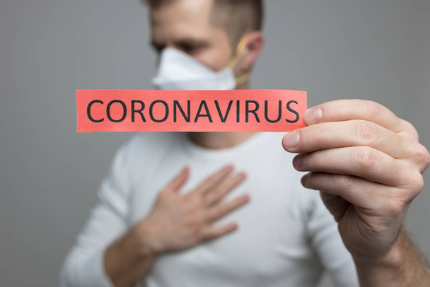 Worried man wearing a respiratory mask, holding the Coronavirus Covid-19 sign - 写真・画像
