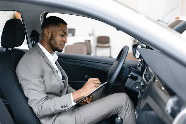 Ο άνθρωπος λαμβάνοντας σημειώσεις που κάθεται σε οδηγούς κάθισμα στην αυτοκινητοβιομηχανία - Φωτογραφία, εικόνα