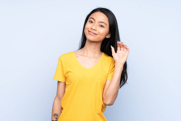 Teenager Chinese woman isolated on blue background saluting with hand with happy expression - Photo, Image