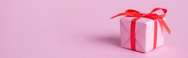 панорамний знімок маленького паперового подарунка зі стрічкою та бантом на рожевому
  - Фото, зображення
