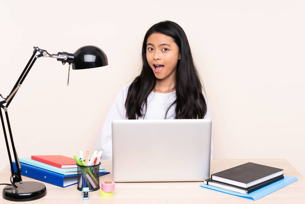 Студентська азіатська дівчина на робочому місці з ноутбуком ізольована на бежевому фоні з несподіваним виразом обличчя
 - Фото, зображення