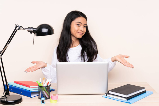 Student asian girl in a workplace with a laptop isolated on beige background smiling - Foto, Imagen