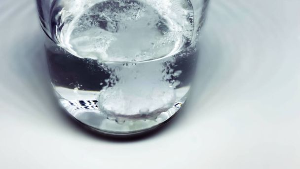 eine Brausetablette, während sie in einen mit Wasser gefüllten Glasbecher fällt. Blasen und prickelnde Wirkung. Medizin und pharmazeutische Mittel - Foto, Bild