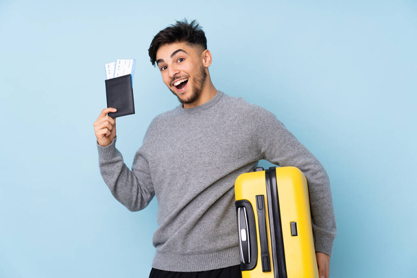 Арабский красивый мужчина изолирован на голубом фоне в отпуске с чемоданом и паспортом - Фото, изображение