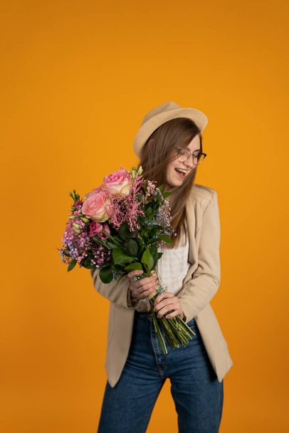 Stylish girl holding flowers and laughing isolated on yellow background - Foto, Bild