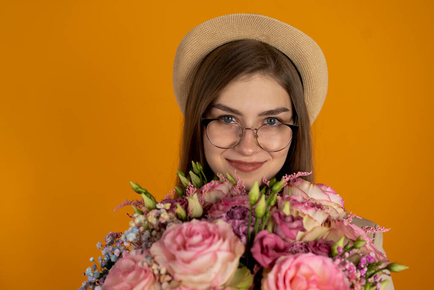 Joyful girl in hat holding eustoma flowers isolated on yellow background - Fotoğraf, Görsel