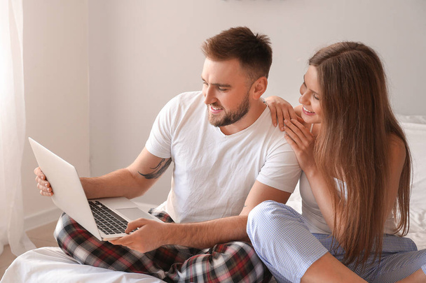 Happy young couple with laptop in bedroom - 写真・画像