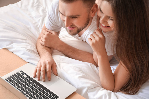 Glückliches junges Paar mit Laptop im Schlafzimmer - Foto, Bild
