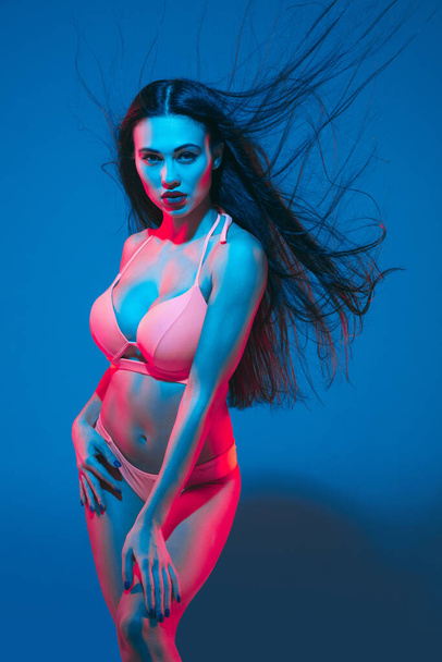 Attractive brunette model on blue studio background in neon light - Foto, Imagem