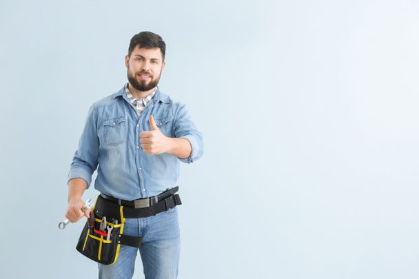 Handsome plumber showing thumb-up on color background - Foto, Imagen